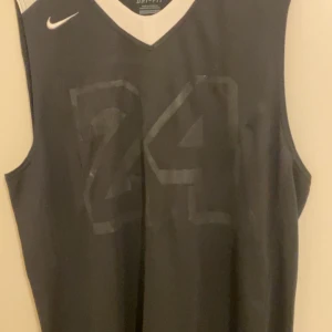Svart basketlinne Nike Dri-Fit XL - Säljer ett svart basketlinne från Nike Dri-Fit i storlek XL. Linnet har nummer 24 och namnet 'BASS' tryckt på ryggen. Tillverkat i ett lätt och ventilerande funktionsmaterial som passar perfekt för träning och sport.