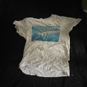 Vit Surfers Paradise t-shirt Surf Tees - Vit t-shirt från Surf Tees Australia med tryck av Surfers Paradise i blå toner på bröstet. Klassisk passform och korta ärmar, perfekt för en avslappnad stil. Tillverkad i mjuk bomull som känns skön mot huden.