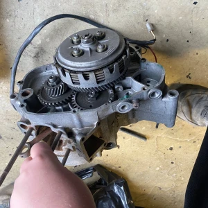 Moped - Denna bild visar en delvis isärplockad motor eller växellåda, troligen från en moped eller motorcykel. Flera kugghjul och kopplingskorg är synliga. Produkten är begagnad och visar tecken på användning och slitage. Perfekt för reservdelar eller renoveringsprojekt.