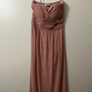 Lång rosa klänning Chiara Forthi - Romantisk långklänning i puderrosa från Chiara Forthi. Klänningen är axelbandslös med draperad överdel och smockad rygg för en bekväm passform. Flödande kjol i lätt tyg som ger en elegant siluett. Perfekt för speciella tillfällen.