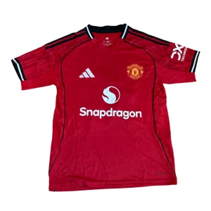 Manchester United Cunha #10 matchtröja - Röd Manchester United fotbollströja från Adidas med tryck 'Cunha 10' på ryggen. Tröjan har klubbmärke på bröstet, vita och svarta detaljer samt sponsorlogga på framsidan. Tillverkad i lätt och ventilerande polyester, perfekt för match eller träning.