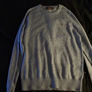 Grå merinoulltröja från Morris XS - Säljer en stilren grå tröja från Morris i 100% merinoull. Tröjan har rund halsringning, ribbade muddar och en liten broderad logga på bröstet. Perfekt för dig som gillar klassisk och enkel stil.