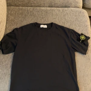 Svart Stone Island t-shirt med patch - Svart t-shirt från Stone Island med klassisk rund hals och ikonisk avtagbar patch på vänster ärm. Den är sprillans ny och oanvänd.