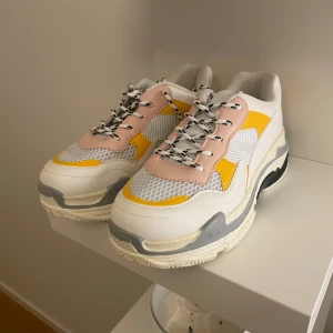 Chunky sneakers i vitt, rosa och gult - Säljer ett par chunky sneakers med vit bas, detaljer i ljusrosa och gult samt grå inslag. Ovandelen är i mesh och syntet med coola svarta och vita snören. Skorna har en tjock, mönstrad sula som ger extra attityd till din outfit.
