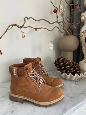 Fila kängor stl 38 – bruna, i mycket fint skick - Säljer ett par Fila kängor i storlek 38 – dam, i mycket fint skick och sparsamt använda. Snygga bruna kängor med fina detaljer som gör dem lätta att matcha till både vardag och mer uppklädda tillfällen. Stadiga, bekväma och perfekta för dig som vill ha både stil och funktion i samma sko. Redo för många nya steg framåt.  Pris: 500 kr  Notera: Snörena är lite nötta på några ställen, inget som syns på håll – se sista bilden.  (Sökord: Fila kängor stl 38 dam bruna skor boots)