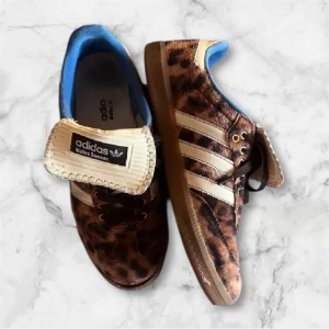 Adidas Wales Bonner leopard sneakers - Färgen är ljusare i verkligheten! Unika Adidas Wales Bonner sneakers med leopardmönster i brunt och svart, vita ränder och blå insida. Skorna har snörning, platt gummisula och detaljer i mocka och skinn. Perfekt för dig som vill sticka ut med coola och trendiga sneakers.