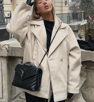 Beige oversized kappa NA-KD - Säljer en beige oversized kappa med dubbelknäppning. Materialet känns mjukt och har en ull-liknande finish. Snygg att matcha med svarta accessoarer.  Slutsåld på NA-KD. Oversize fit.