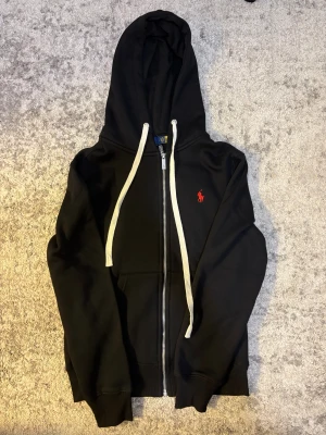 Ralph lauren hoodie - En snygg svart hoodie från polo Ralph lauren med en röd logga på bröstet. Storleken är S men passar som XS.