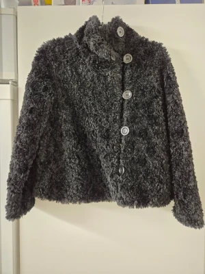 Teddyjacka - Mysig svart teddyjacka från Lindex med hög krage och stora knappar framtill. Jackan har fluffig pälslook och är perfekt för kyliga dagar. Rak passform och långärmad modell som ger en cool vibe till din outfit.