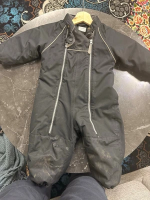 Svart täckbyxa Friends med dragkedja - Svarta täckbyxor från Friends med två snedställda dragkedjor framtill och reflexdetaljer. Insidan är fodrad med mjuk fleece för extra värme. Elastisk midja bak och muddar vid benslut. Perfekt för kalla dagar utomhus.