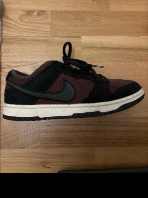 Nike Dunk Low mörkbruna sneakers - Nike Dunk Low sneakers i mörkbrunt och svart med grov mocka på ovandelen. Klassisk rund tå, svart swoosh och snörning. Vit mellansula och svart yttersula ger en snygg kontrast. Perfekt för dig som gillar streetwear och unika material. Skicka dm om du vill ha mer bilder.