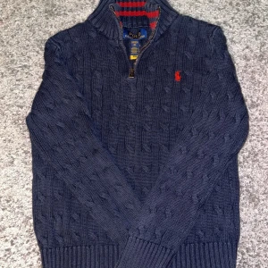 Mörkblå stickad tröja Polo Ralph Lauren skriv för pris förslag  - Kabelstickad mörkblå tröja från Polo Ralph Lauren med halv dragkedja och röd broderad logga på bröstet. Tröjan har hög krage, långa ärmar och ribbade muddar. Perfekt för kyliga dagar och snygg till jeans. 