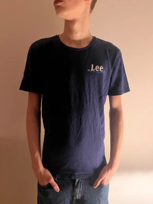 Mörkblå t-shirt från Lee - Snygg mörkblå t-shirt från Lee med vit logga tryckt på bröstet. Klassisk rund halsringning och korta ärmar. Tillverkad i mjuk bomull som känns skön mot huden. Perfekt för en clean och enkel stil.