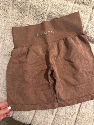 Bruna seamless shorts från NVGTN - Säljer ett par bruna seamless shorts från NVGTN med hög midja och bred resår. De är stretchiga och perfekta för träning, tillverkade i en mjuk blandning av nylon och spandex. Snygg, enkel design utan mönster och med diskret logga framtill.