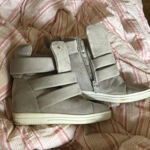 Gråa Isabel Marant liknande wedge sneakers  - Snygga grå sneakers med inbyggd kilklack från Siader. Skorna har flera breda band, dragkedja på sidan och är gjorda i mjuk mocka-look. Vit platt sula och rund tå ger en cool streetstil. Perfekta för dig som vill ha lite extra höjd men ändå sneakers-vibe.