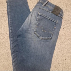 Replay blå jeans herr 29/30 - Säljer ett par snygga blå jeans från Replay i klassisk tvätt. Modellen har fem fickor, diskreta slitningar och raka ben. Jeansen är tillverkade i bomull och har Replay-logga på bakfickan. Perfekta för dig som gillar en tidlös look.