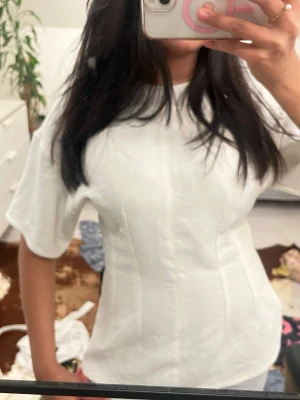 Vit korsett-topp från Zara XS - Säljer en vit topp från Zara i storlek XS. Toppen har korta ärmar och markerade sömmar som ger en snygg formad siluett. Materialet är mjukt och har en lätt struktur, perfekt för dig som gillar stilrena och trendiga plagg.