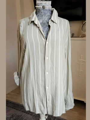 Grön randig oversized skjorta - Snygg grln skjorta med vita vertikala ränder och klassisk krage. Skjortan har en oversized passform, långa ärmar och knäppning framtill.