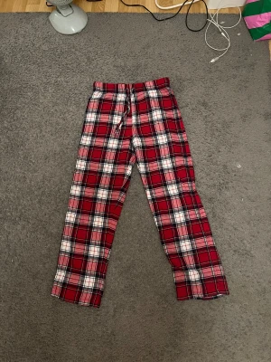 Rödrutiga mjukisbyxor med snörning - Rödrutiga mjukisbyxor från C i storlek 146/152. Byxorna har ett klassiskt rutmönster i rött, vitt och svart samt snörning i midjan för extra komfort. Perfekta för chill dagar hemma eller som mysplagg.