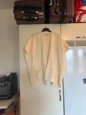 Vit stickad kofta från Cream - Mysig vit stickad kofta från Cream i oversized modell. Koftan har ribbade muddar, två framfickor och ett snyggt randigt mönster i stickningen. Perfekt att slänga över en t-shirt när det är lite kyligt ute. Passar dig som gillar avslappnad stil. Storlek One Size men den är väldigt oversize.  Mycket fint skick, jag hittar inga synliga anmärkningar eller defekter. 