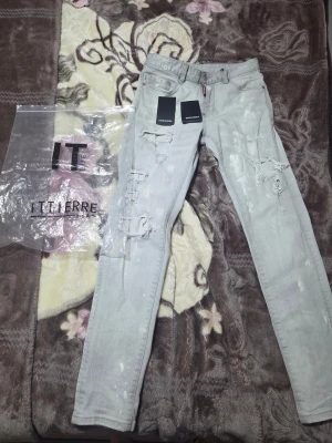 Ljusa slitna jeans från Dsquared2 - Säljer ett par ljusgrå jeans från Dsquared2 med coola slitningar och färgstänk. Skinny fit med klassisk femficksdesign och dragkedja med Dsquared2-detalj. Perfekta för dig som gillar streetstyle och vill sticka ut.