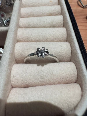 Silverfärgad ring med blomma - En söt och stilren ring i silverfärg med en liten blomma som detalj framtill. Ringen har en tunn, rund form och blommans kronblad är tydligt markerade för en charmig look. Perfekt accessoar för dig som gillar enkla men unika smycken.