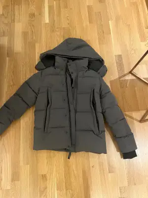 Säljer en mörkgrå pufferjacka i storlek S. Jackan har huva, dragkedja och knappar framtill, samt två stora fickor på sidorna. Perfekt för kalla dagar med sin tjocka och quiltade design. Stilsäker och funktionell för vintern.