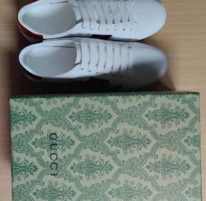 Gucci Ace vita sneakers med orm - Säljer ett par vita Gucci Ace sneakers i skinn med klassiska gröna och röda ränder på sidan samt broderad orm i rött, svart och vitt. Baksidan har metallicdetaljer i rött och grönt med Gucci-logga. Skorna har snörning och platt sula. Box medföljer.och andvönda en gång