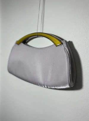 Retro satinväska - unik festväska - Fin liten väska i syntetisk satin, perfekt för fest eller vardag. Väskan har ett tjock snöre som axelband och unikt handtag, men materialet har lite matthet och lätt nopprighet, vilket är normalt för satin. Säljer då den står mest i garderoben och tar plats.  Väskan är rentvättad, men en svag antydan av tidigare fläck finns kvar (syns bara vid nära granskning).  Det finns tre små hål på undersidan, som inte syns vid användning, därmed har jag valt lägre pris.  påverkar dock inte helhetsintrycket