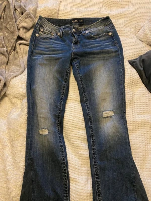 Miss Me blå bootcut jeans strl 29 - Snygga blå jeans från Miss Me med bootcut passform och slitna detaljer på benen. Jeansen har dekorativa bakfickor med broderier och metallknappar med blommönster. Klassisk femficksmodell och kontrastsömmar för extra edge. Det är mer midwaist hade kunnat sänka till 750 