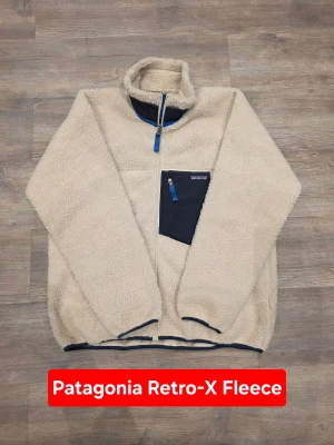 Patagonia Classic Retro-X Fleece Jacket Beige Boxy Fit Outdoor - Iconic Patagonia fleece with that clean retro outdoor look everyone wants right now. Patagonia Classic Retro-X full zip fleece in a timeless beige colorway with contrast chest pocket. Thick pile fleece, boxy fit and wind-blocking lining make it both functional and stylish. Perfect for streetwear, workwear layering or everyday winter wear.  Measurements: Length (A): 72 cm Width / Chest (D): 68 cm Shoulder-to-cuff (B): 61 cm Pit-to-cuff (C): 56 cm  Condition: New without tags Size: XL