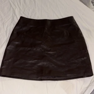 Brun kortkjol i skinnimitation H&M - Snygg brun kortkjol från H&M i skinnimitation med en stilren och rak passform. Kjolen har dragkedja bak och är tillverkad i polyester. Perfekt för dig som gillar en edgy och trendig look.