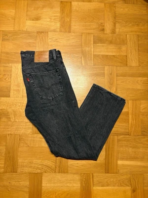Levis 501 svarta  - Tja sväljer ett par svarta Levis 501 31W 30L. De är raka i passformen för en klassisk look. Vid minsta fråga är det bara att höra av sig.