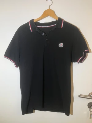 Svart Moncler piké polo - Svart polotopp från Moncler med klassisk krage och knappar framtill. Storlek S/M, nytt skick!