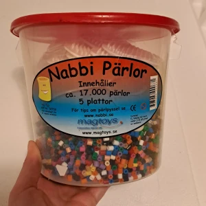 Hink med pärlor och pärlplattor - 1/3 fylld hink nabbi pärlor i olika färger, med 22 pärlplattor!! 4 sexhörninga, 4 kvadrater, 3 äggformader, 2 runda, 3 stjärnor, 2 hjärtan, en nalle, 2 barn en flicka och en pojke och en kyckling, 3 pärlplattor har gulnat lite men funkar precis lika bra, perfekt julklapp👌🏼Hoppas det intresserar!