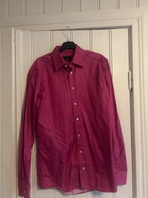 Rosa slim fit skjorta från Eton - Snygg rosa skjorta från Eton i slim fit-modell. Skjortan har klassisk krage, långa ärmar och vita knappar framtill. Perfekt för dig som vill sticka ut med färg och stil. Materialet är mjukt och känns lyxigt mot huden.