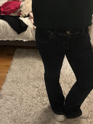 Mörkblå bootcut jeans från Cross - Snygga mörkblå jeans från Cross Jeanswear Co. med klassisk bootcut passform och kontrastsömmar. Jeansen har fem fickor och cool broderad detalj på bakfickorna. Perfekt för dig som gillar en tidlös look med lite extra edge.