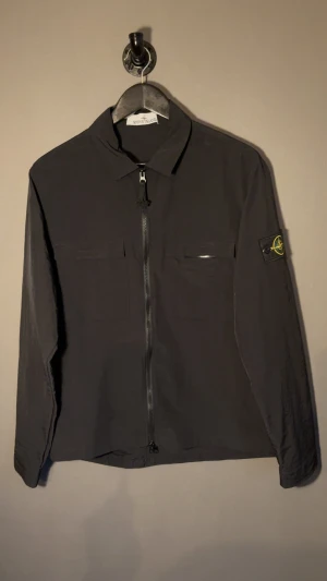 Svart overshirt från Stone Island - Svart overshirt från Stone Island med klassisk krage, funkar som jacka eller bara som en lättare tröja under en jacka! Hör av dig vid frågor!🙏