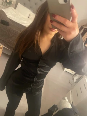 Svart figursydd skjorta i satin - Snygg svart skjorta i glansigt satinliknande material med figurnära passform. Denna är skräddarsydd för att få den figurnära passformen. Skjortan var i storlek xs men skulle nu vilja säga att den är insydd till ungefär en xxs  