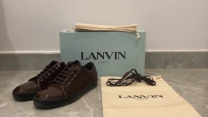 Bruna sneakers från Lanvin i mocka - Snygga bruna sneakers från Lanvin med ovandel i mjuk mocka och cap toe framtill. Skorna har rund tå, platt svart sula och klassisk snörning. Kommer med originalkartong, dustbags, extra laces och kvitto. Perfekta för dig som gillar stilrena och lyxiga sneakers. Kom privat för fler bilder, priset är diskuterbart❄️