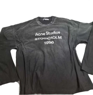  Acne Studios tröja  - Trendig svart långärmad tröja från Acne Studios med den klassika vita texten 'Acne Studios Stockholm 1996' på bröstet. Har en relaxed fit och är perfekt för en stilren och avslappnad look. Passar med allt. 