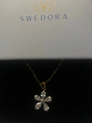 Halsband från swedora -  halsband från Swedora med ett blommigt hänge i guld och glittrande stenar. Aldrig använt. Priset går att diskutera. Ny pris 350kr