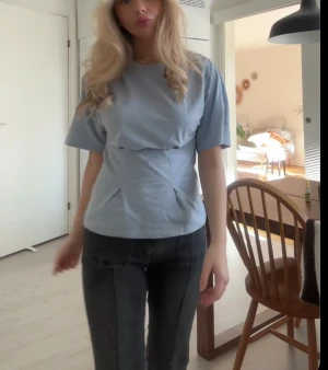 Ljusblå blus med veck - Säljer en ljusblå blus med coola veckdetaljer framtill som ger en unik form. Blusen har rund hals, korta ärmar och är gjord i mjuk bomull. Perfekt för dig som gillar minimalistisk stil med en twist.