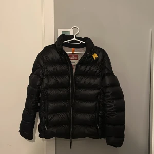 Svart pufferjacka Parajumpers XS - Säljer en svart pufferjacka från Parajumpers i storlek XS. Jackan har en glansig finish, markerad krage och cool gul detalj vid halsen. Fodret är grått och jackan har dragkedja framtill samt praktiska fickor. Perfekt för kalla dagar och har en modern, puffig look.