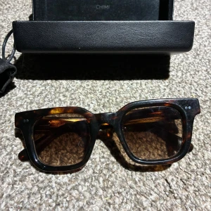 CHIMI lab 04  - Snygga solglasögon från CHIMI i modellen LAB 04 Havana. Ramen är fyrkantig och har ett brunt och svart mönster som ger en cool tortoise-look. Glasen är mörka och passar perfekt för soliga dagar. Kommer med originalfodral och tygpåse med CHIMI-logga. Använt få antal gånger.