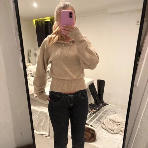 Beige stickad hoodie - Säljer en beige stickad hoodie med huva och snörning. Tröjan har bred ribbad midja och långa ärmar med avslappnad passform. Perfekt för dig som gillar en chill och trendig look. Passar till både jeans och kjol. Tröjan är ifrån ginas barn avdelning och har sytt in den själv i midjan 