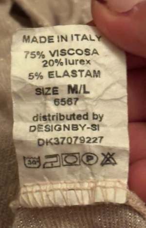 Glittrig beige långärmad topp Design by Si - Säljer en beige långärmad topp från Design by Si med glittrigt lurexmaterial. Toppen har en bred, något offshoulder ringning och är figurnära i passformen. Materialet är mjukt och stretchigt med en skimrande finish som ger en extra touch.