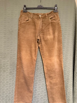 Morris Manchesterbyxor - Säljer ett par snygga  manchesterbyxor från Morris. Byxorna har rake ben och normal passform. Tillverkade i mjuk manchester med tydlig struktur och detaljer som logoknapp och läderpatch bak. Jättefint skick, enda skavanken är ett litet hål på baksidan av ena benet (se bild 6). Storlek 33/33. Längd: ca 104cm, innerbenslängd: ca 79cm, midja: ca 44cm, benslut: ca 20cm. 