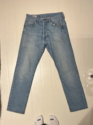 Levi's 501 ljusblå jeans W30 L32 - Klassiska Levi's 501 Premium jeans i ljusblå tvätt. Rak passform med fem fickor, knappgylf och snygga kontrastsömmar. Perfekta för en avslappnad och tidlös look. Tillverkade i slitstarkt bomullsjeans.
