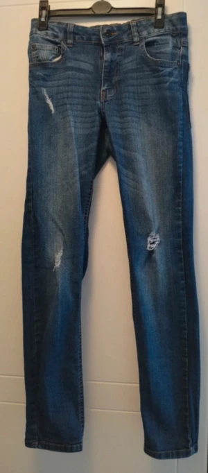 Pojk jeans - Snygga blå jeans med skinny passform och coola slitningar på benen. Klassisk femficksmodell med normal midja och dragkedja. Jeansen har en mörkblå tvätt med lätt faded effekt och är gjorda i stretchigt denim för skön komfort.